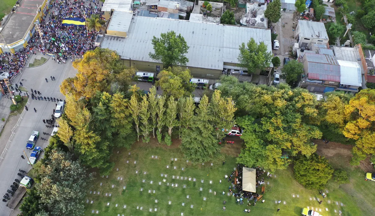 Kerabat dan teman menguburkan jenazah Diego Maradona, sementara polisi menjaga penggemar di luar pemakaman Jardin de Bellavista di Buenos Aires, Kamis (26/11/2020). Maradona meninggal dunia dalam usia 60 tahun pada Rabu (25/11) karena serangan jantung. (AP Photo/Rodrigo Abd)
