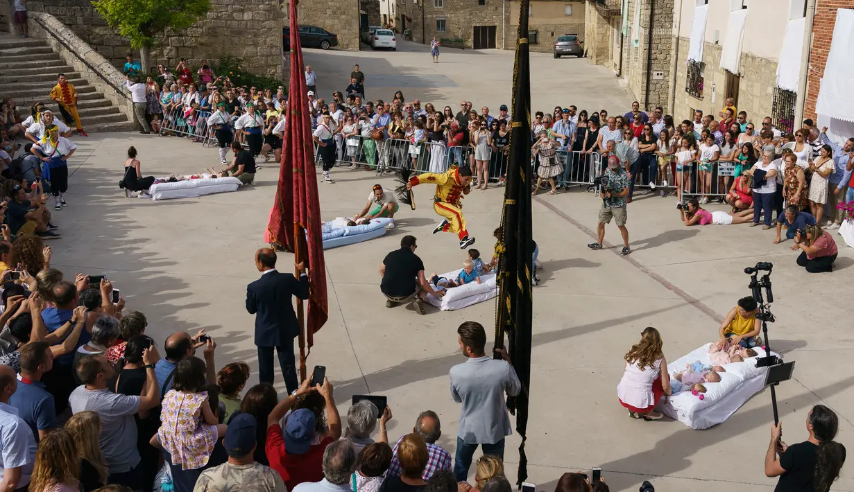 Pria berkostum setan melompati bayi-bayi yang terlentang di atas matras di sebuah jalan selama festival El Colacho di desa Castrillo de Murcia, bagian utara Spanyol, 23 Juni 2019. Adapun bayi yang dijajarkan dan dilompati 'El Colacho' telah mendapat izin dari orangtua sang bayi. (CESAR MANSO/AFP)