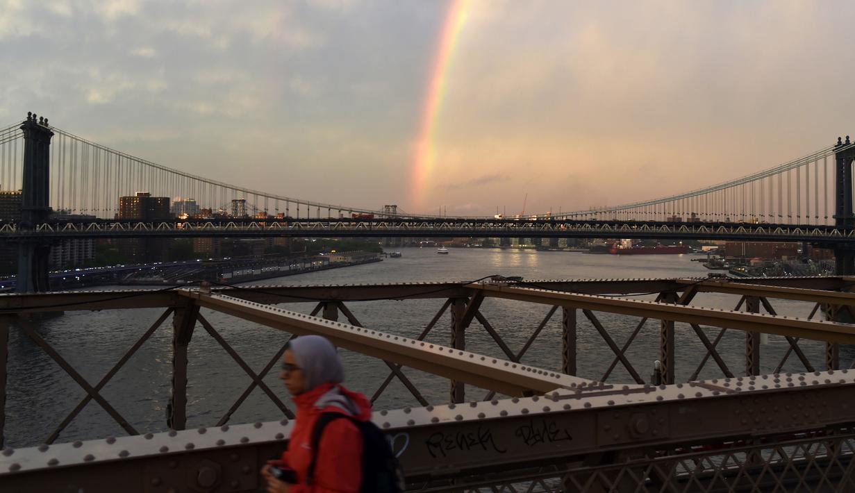 Warga beraktivitas saat pelangi terlihat dari Jembatan Brooklyn di New York City, AS (15/5). Jembatan ini adalah jembatan suspensi terpanjang di dunia sejak pembukaannya hingga 1903, serta jembatan suspensi kabel baja pertama. (AFP Photo/Hector Retamal)