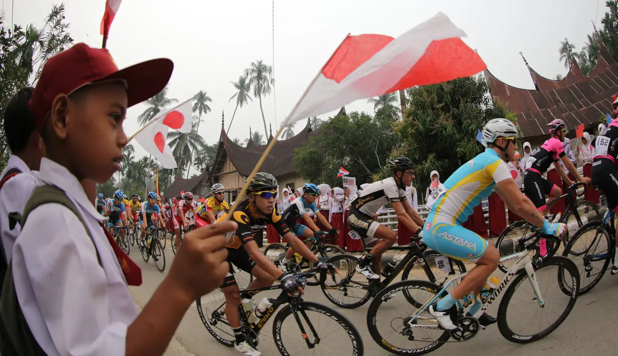 Para pebalap di sambut murid-murid SD sesaat setelah start dari Desa Adat Sijunjung dalam Etape 3 Tour de Singkarak 2015 antara Sijunjung menuju Dharmasraya, Sumatra Barat, Senin (5/10/2015). (Bola.com/Arief Bagus)