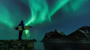 Seorang surfer melihat Cahaya Utara atau aurora borealis di Utakleiv, Norwegia utara (9/3). Aurora ini adalah sebuah peristiwa langit yang cantik berupa pancaran cahaya yang menyala-nyala di atmosfer sekitar lingkaran Arktik. (AFP/Olivier Morin)