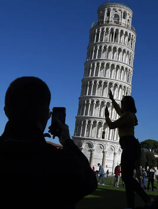 Turis berpose di depan Menara Pisa di kota Pisa, Italia pada 28 November 2018. Setelah upaya yang dilakukan selama lebih dari dua puluh tahun, para insinyur mengatakan kemiringan menara setinggi 57 meter itu telah berkurang 4 cm. (Tiziana FABI / AFP)