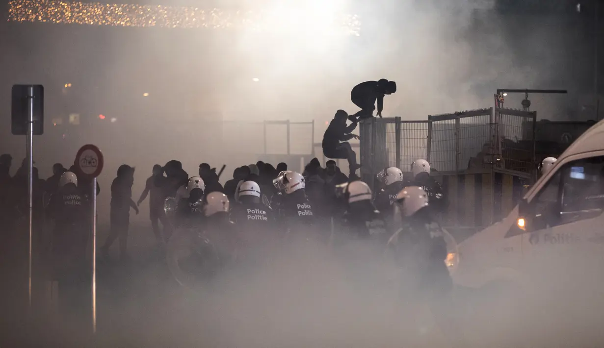Petugas polisi anti huru hara Belgia bentrok dengan pendukung Maroko setelah timnas kesayangan mereka kalah dari Prancis pada laga semifinal Piala Dunia 2022, di Brussel, Belgia, Rabu (14/12/2022). Mereka juga membakar beberapa kantong sampah dan kotak kardus. (Simon Wohlfahrt / AFP)