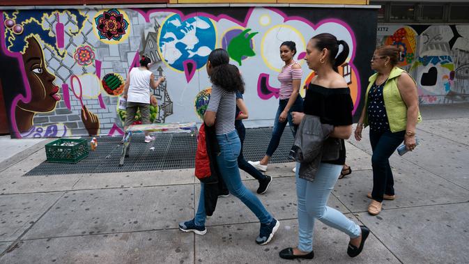 Sekelompok wanita berjalan melewati seniman grafiti Sandra Fabara atau lebih dikenal Lady Pink yang tengah melukis mural di Casita Maria, Bronx, New York, AS, Minggu (2/6/2019). Di usianya yang sudah menginjak 50 tahun, Lady Pink mencari nafkah dengan karya seninya secara legal. (Don Emmert/AFP)