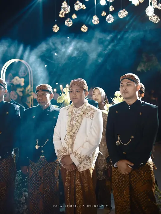 Denny Caknan dan Bella Bonita memilih adat Jawa yang kental, lengkap dengan penggunaan busana, riasan, dan aksesorinya. Keduanya memilih nuansa warna putih untuk busana pengantin, dengan sentuhan payet emas yang mewah. Foto: Instagram.