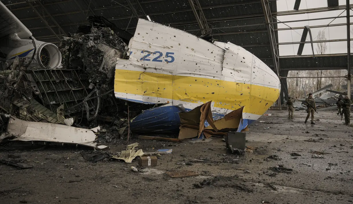Prajurit Ukraina melewati pesawat Antonov An-225 Mriya yang hancur di bandara Antonov, Hostomel, 2 April 2022. Di pintu masuk Bandara Antonov, pasukan menjaga posisinya, tanda mereka memegang kendali penuh atas landasan pacu yang coba diserbu Rusia di hari-hari pertama perang (AP Photo/Vadim Ghirda)