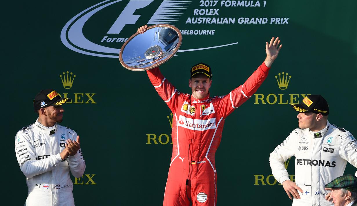 Pembalap Ferrari, Sebastian Vettel berpose dengan trofinya setelah memenangi balapan GP Australia di Sirkuit Albert Park, Melbourne, Minggu (26/3). Pembalap asal Jerman tersebut sukses mengalahkan pesaing terberatnya Lewis Hamilton. (WILLIAM WEST/AFP)