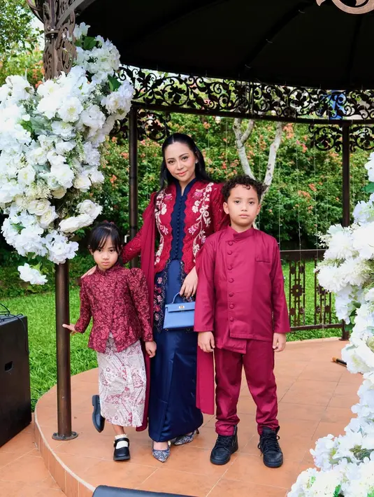 Ibu dua anak ini kenakan kebaya merah biru navy dengan motif bordir floral dan selendang bahu. Rok panjang biru satin lengkapi tampilan anggunnya [@rachelvennya]