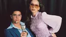 Dalam foto ini, Al Ghazali duduk di kursi dengan mengenakan setelan jas biru tua yang khas, lengkap dengan kemeja berkerah lebar yang terbuka. Dengan tatapan tajam, ia memegang tongkat yang mirip dengan gaya Elvis Presley, menambah kesan berani dan karismatik. Di sampingnya, Alyssa Daguise tampil anggun dalam balutan atasan ungu muda yang bertekstur, mengingatkan kita pada gaya Priscilla yang ikonik. (Liputan6.com/IG/@alyssadaguise)