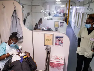 Seorang dokter gigi merawat seorang pasien ketika seorang perawat berjalan di atas kereta Phelophepa, yang diparkir di stasiun kereta Dube di Soweto, pada tanggal 17 Oktober 2023. (EMMANUEL CROSET/AFP)