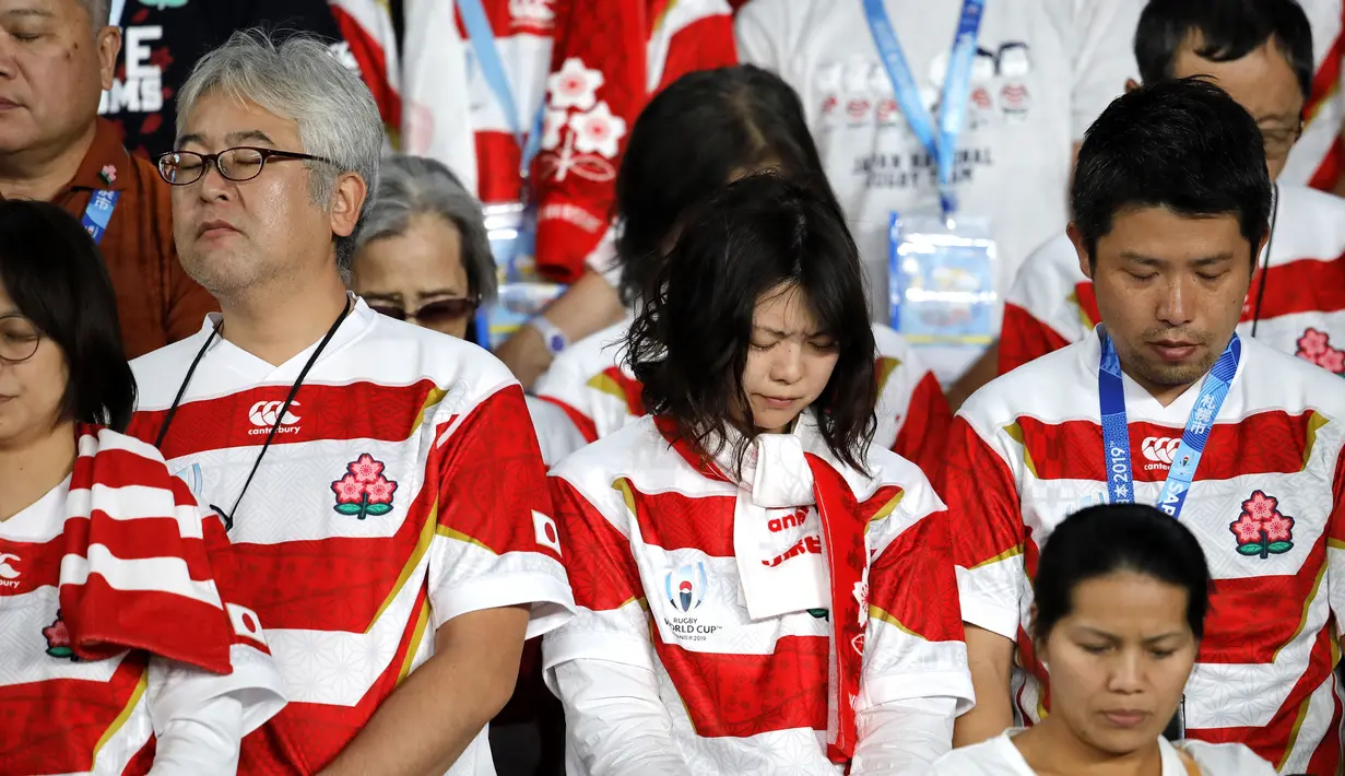 Suporter Jepang berdoa untuk para korban Topan Hagibis sebelum pertandingan melawan Skotlandia di Piala Dunia Rugbi 2019 Jepang di Stadion Internasional Yokohama (13/10/2019). Topan Hagibis membuat sebagian wilayah Jepang lumpuh. (AP Photo/Christophe Ena)