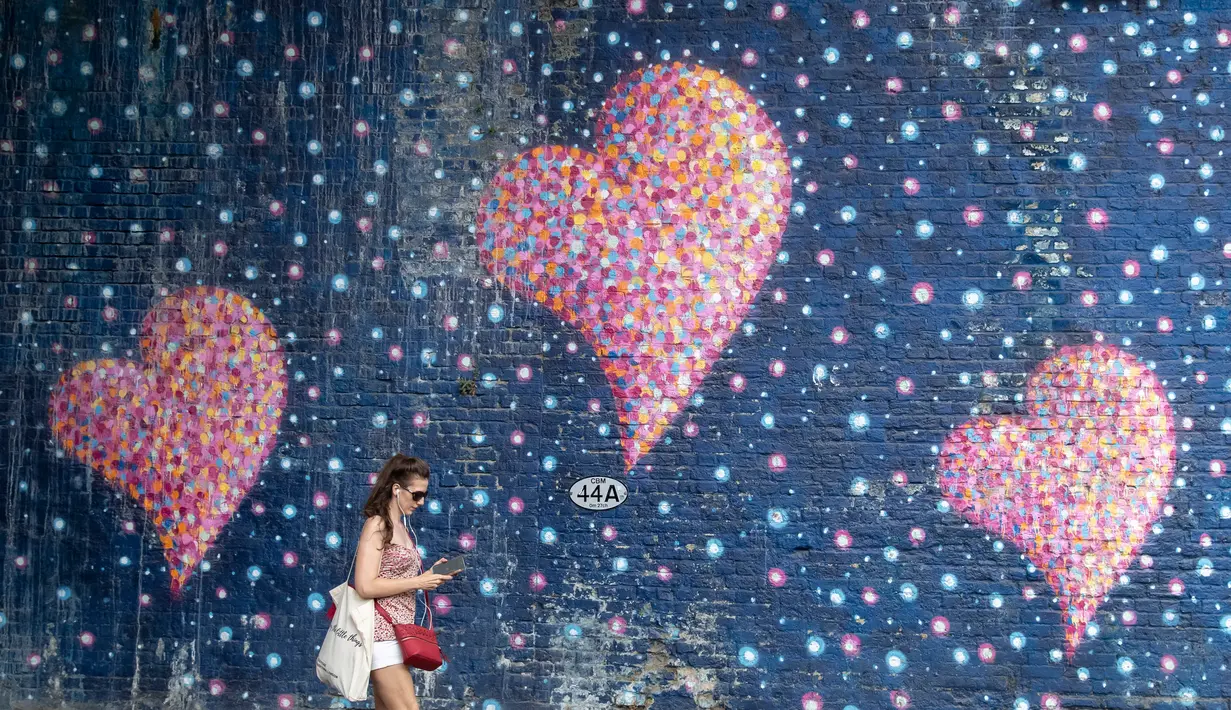 Seorang perempuan melewati lukisan mural lambang cinta di London, Inggris, pada 1 Agustus 2020. Pemerintah Inggris pada Jumat (31/7) mengumumkan penundaan pelonggaran beberapa langkah pembatasan menyusul jumlah infeksi virus corona yang meningkat. (Xinhua/Han Yan)