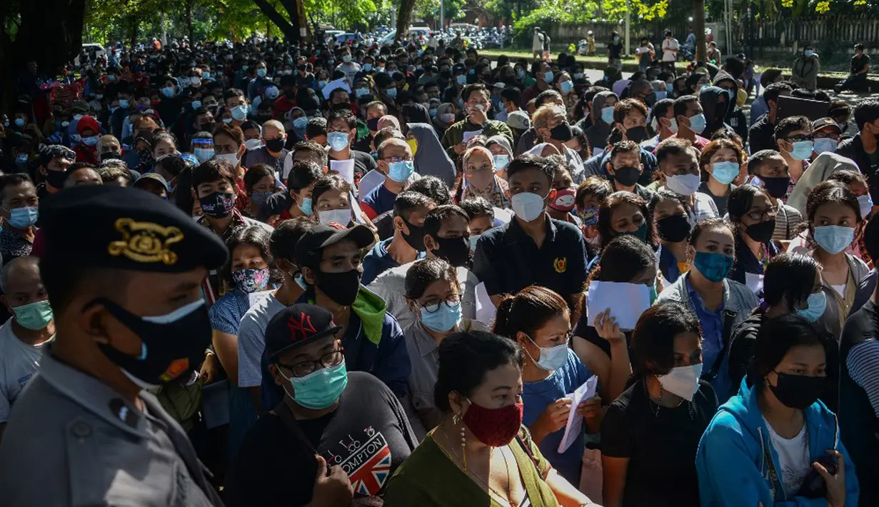 Polisi melakukan pengamanan saat warga menunggu dalam antrean untuk mendaftar vaksin virus corona COVID-19 AstraZeneca di Denpasar, Bali, Sabtu (26/6/2021). Ratusan warga terlihat antusias mengikuti vaksinasi massal ini. (SONY TUMBELAKA/AFP)