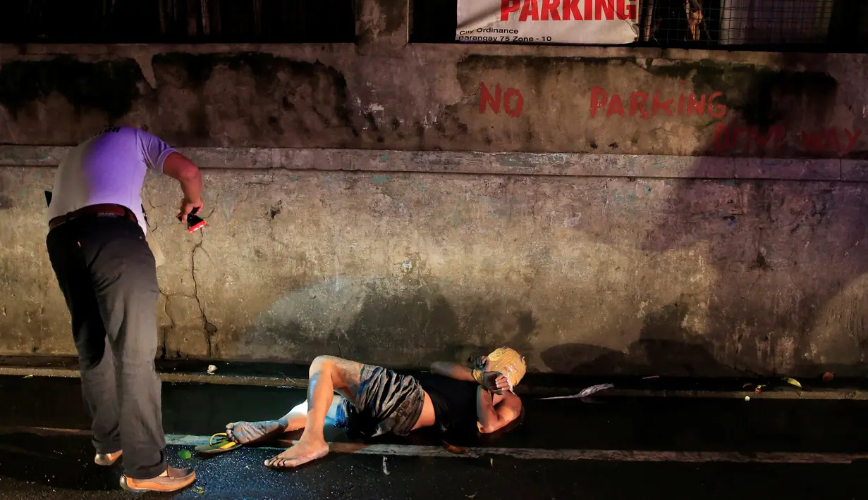 Petugas memeriksa jenazah dengan kondisi kepala terbungkus lakban di pinggir jalan Kota Pasay, Filipina (15/11). Filipina terus membasmi peredaran narkoba dengan cara menembak di tempat bagi pecandu dan pengedar narkoba. (Reuters/Romeo Ranoco)