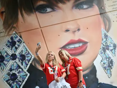 Penggemar Taylor Swift berswafoto dengan latar belakang mural sang penyanyi yang dibuat oleh seniman jalanan MurWalls, di luar Stadion Wembley, London, Kamis (15/8/2024). (JUSTIN TALLIS / AFP)