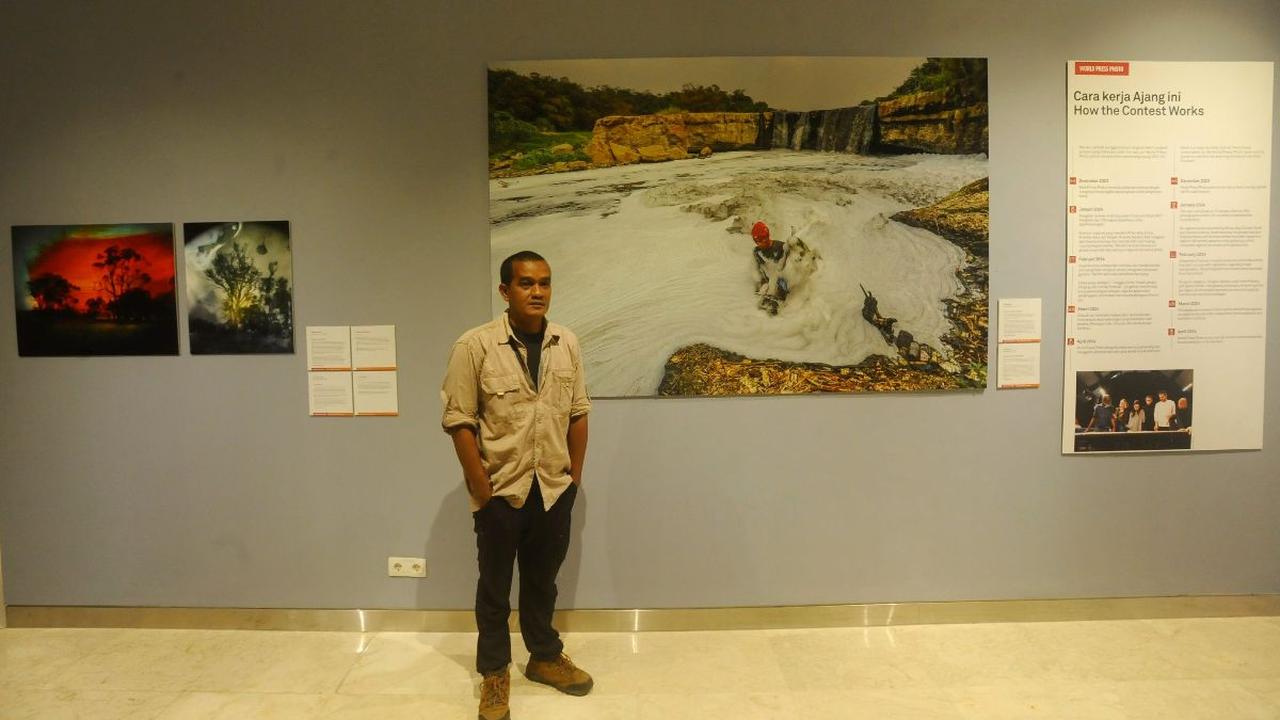 Pewarta Foto Merdeka.com, Arie Basuki berpose di depan karyanya yang berjudul “Pollution in the Cileungsi River” saat pameran World Press Photo (WPP) 2024 di Pusat Kebudayaan Belanda Erasmus Huis, Jakarta, Sabtu (24/8/2024).&nbsp;<br>