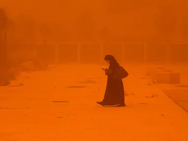 Seorang perempuan melihat-lihat telepon saat berjalan di tengah badai debu yang parah di Kota Kuwait pada 23 Mei 2022. Kabut oranye tebal telah menyelimuti Kuwait pada hari Senin, menyebabkan penerbangan ke dan dari bandara internasional negara itu ditangguhkan sementara, kata regulator penerbangan sipil. (Yasser Al-Zayyat / AFP)