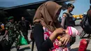 Seorang wanita membawa anaknya ketika mereka tiba di Surabaya, Kamis (4/10). Banyak anak-anak yang terpisah dari keluarganya setelah bencana gempa-tsunami melanda Palu dan Donggala pada 28 September. (AFP Photo/Juni Kriswanto)