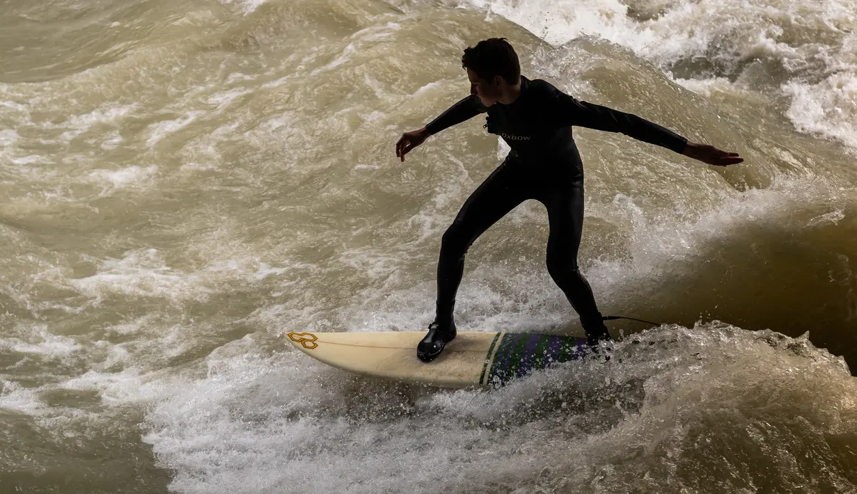 Peselancar berusaha berdiri di atas papan seluncur saat bermain "surfing" di sungai buatan Eisbach di English Garden Munich, Jerman pada 28 Mei 2019. Aliran air sungai Sungai Eisbach yang memiliki lebar 12 meter ini berasal dari Sungai Isar. (Photo by Peter Kneffel/dpa/AFP)