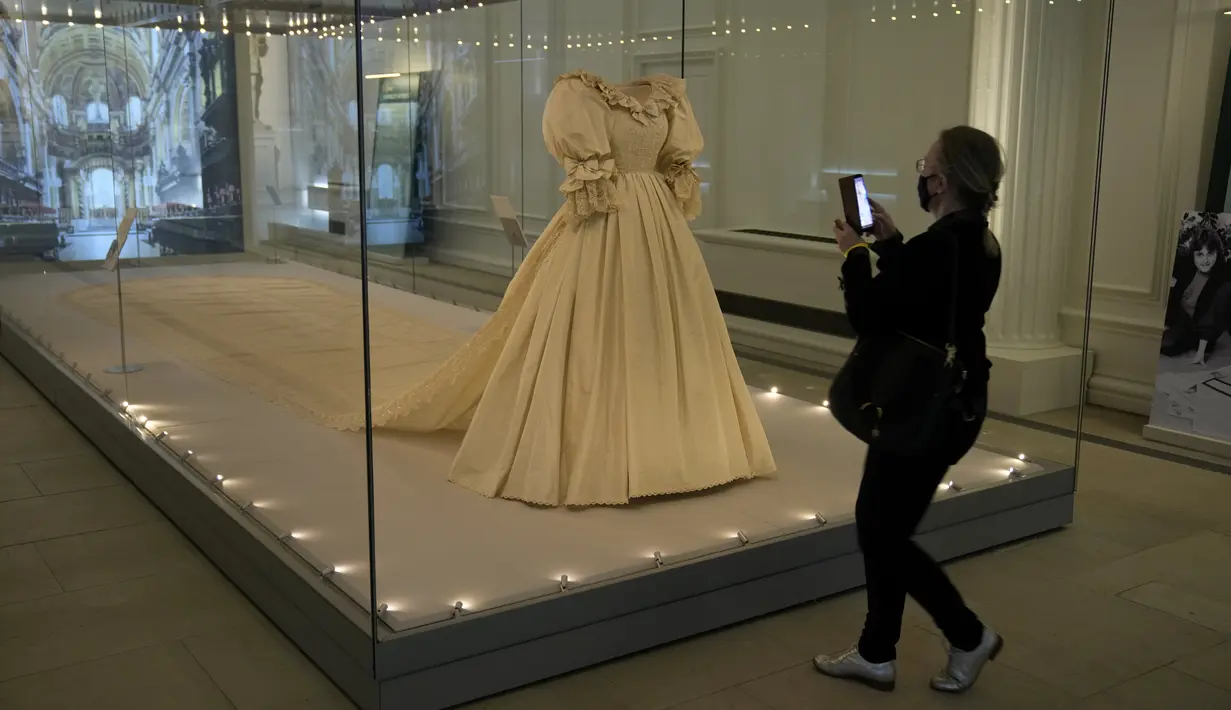 <p>Jurnalis berdiri di samping gaun pengantin Putri Diana selama pratinjau media untuk pameran "Royal Style in the Making" di Istana Kensington di London, Rabu (2/6/2021). Pameran yang dibuka untuk pengunjung pada Kamis, 3 Juni 2021, ini akan berlangsung hingga 2 Januari 2022. (AP Photo/Matt Dunham)</p>