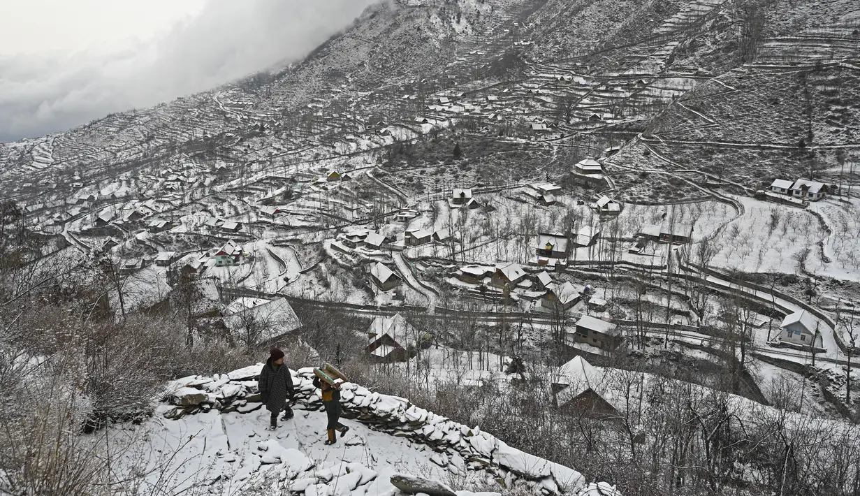 Anak-anak berjalan di atas gunung setelah salju turun di pinggiran Srinagar, Kashmir, India, pada 29 Desember 2020. Hujan salju memutihkan kota utama di Kashmir tersebut. (Photo by Tauseef MUSTAFA / AFP)