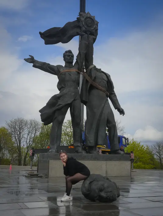 <p>Seorang perempuan berpose untuk foto sambil duduk di atas kepala patung pekerja Soviet selama pembongkaran monumen era Soviet untuk persahabatan antara Rusia dan Ukraina, di tengah invasi Moskow di Kiev tengah, Ukraina, Selasa (26/4/2022). Patung itu terletak di bawah 'Lengkungan Persahabatan Rakyat' titanium raksasa, yang didirikan pada 1982 untuk memperingati ulang tahun ke-60 Uni Soviet. (AP Photo/Efrem Lukatsky)</p>