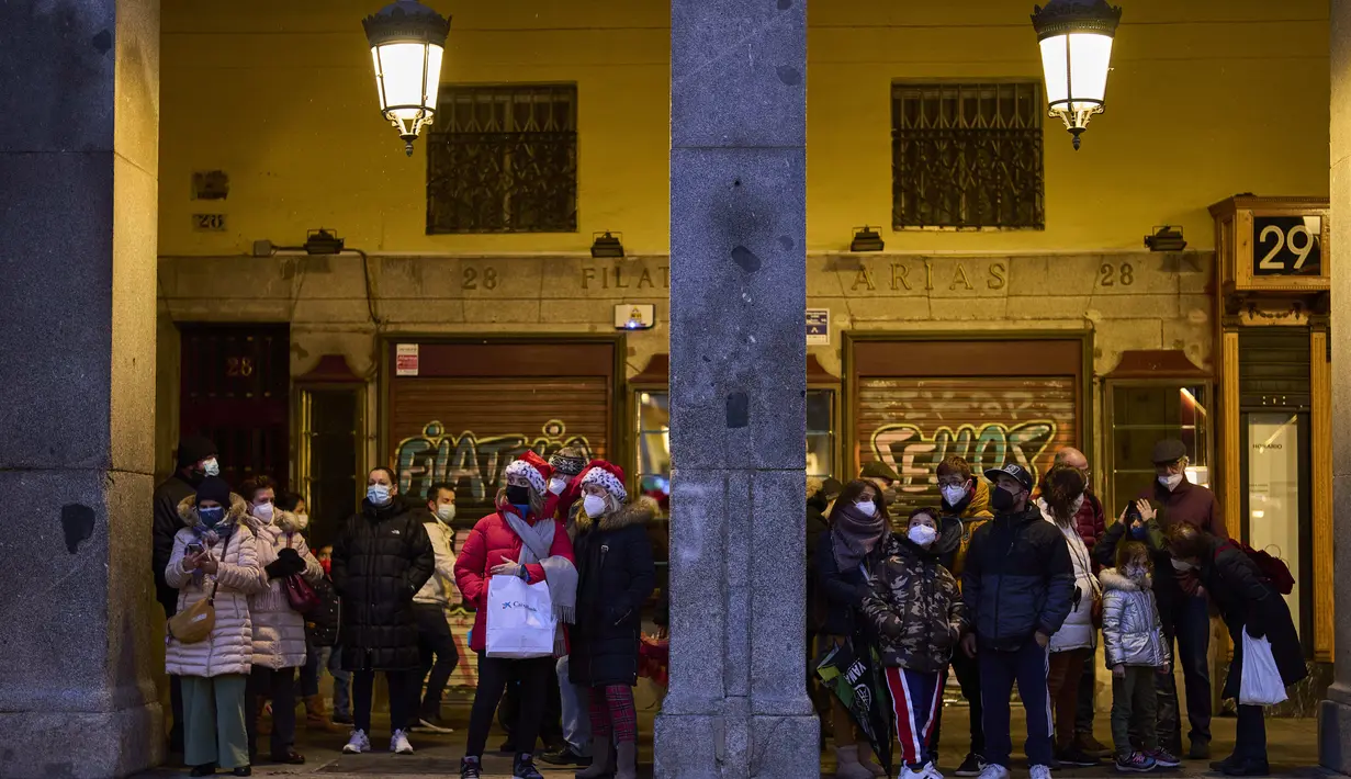 Orang-orang yang memakai masker untuk melindungi diri dari penyebaran virus corona, menunggu hujan berhenti di pusat kota Madrid, Spanyol (8/12/2021). PM Spanyol mendesak warga untuk "tetap berhati-hati" tentang COVID-19 selama liburan perayaan Natal. (AP Photo/Manu Fernandez)