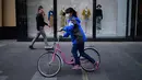 Seorang wanita mengenakan masker mengendarai sepedanya melewati sebuah toko di Beijing (19/4). Beijing memiliki populasi 21.150.000 pada tahun 2013. (AFP Photo/Wang Zhao)