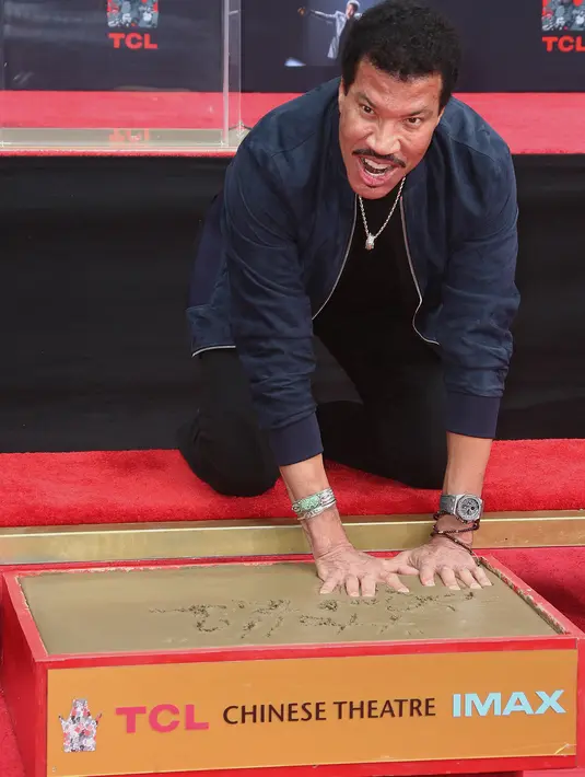 Penyanyi R&B AS, Lionel Richie mencelupkan tangannya di semen sambil tersenyum ke arah kamera di TCL Chinese Theatre, Hollywood, Rabu (7/3). Nama salah satu ikon musik dunia itu juga terpatri di Hollywood Walk of Fame. (Tommaso Boddi/Getty Images/AFP)