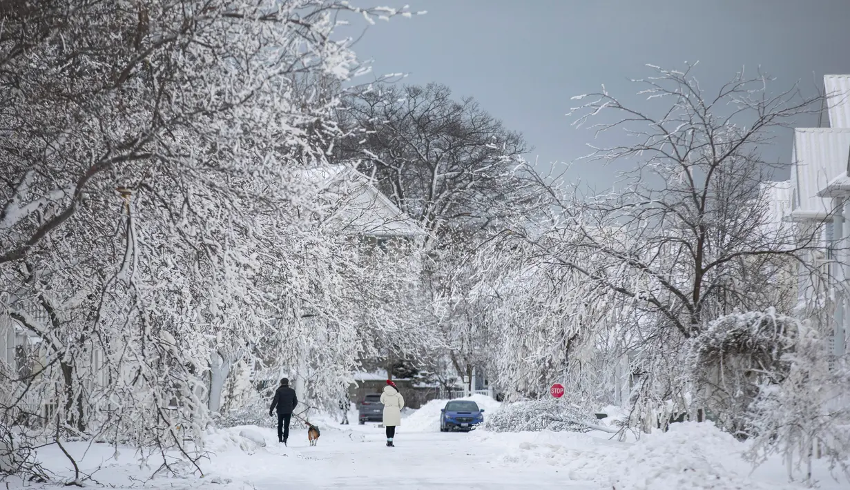 Orang-orang berjalan menyusuri jalan bersalju menyusul badai musim dingin yang melanda sebagian besar Ontario di Fort Erie, Ontario, Kanada, 27 Desember 2022. Kondisi kian buruk dengan suhu yang hampir mencapai minus 45 derajat celcius. (Nick Iwanyshyn/The Canadian Press via AP)