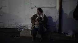 Seorang wanita pengungsi memegang anjingnya duduk di pinggir jalan mendekati perbatasan dengan Polandia di Shehyni, Ukraina, Minggu (6/3/2022). Jumlah orang Ukraina yang dipaksa meninggalkan negara mereka meningkat menjadi 1,5 juta. (AP Photo/Daniel Cole)