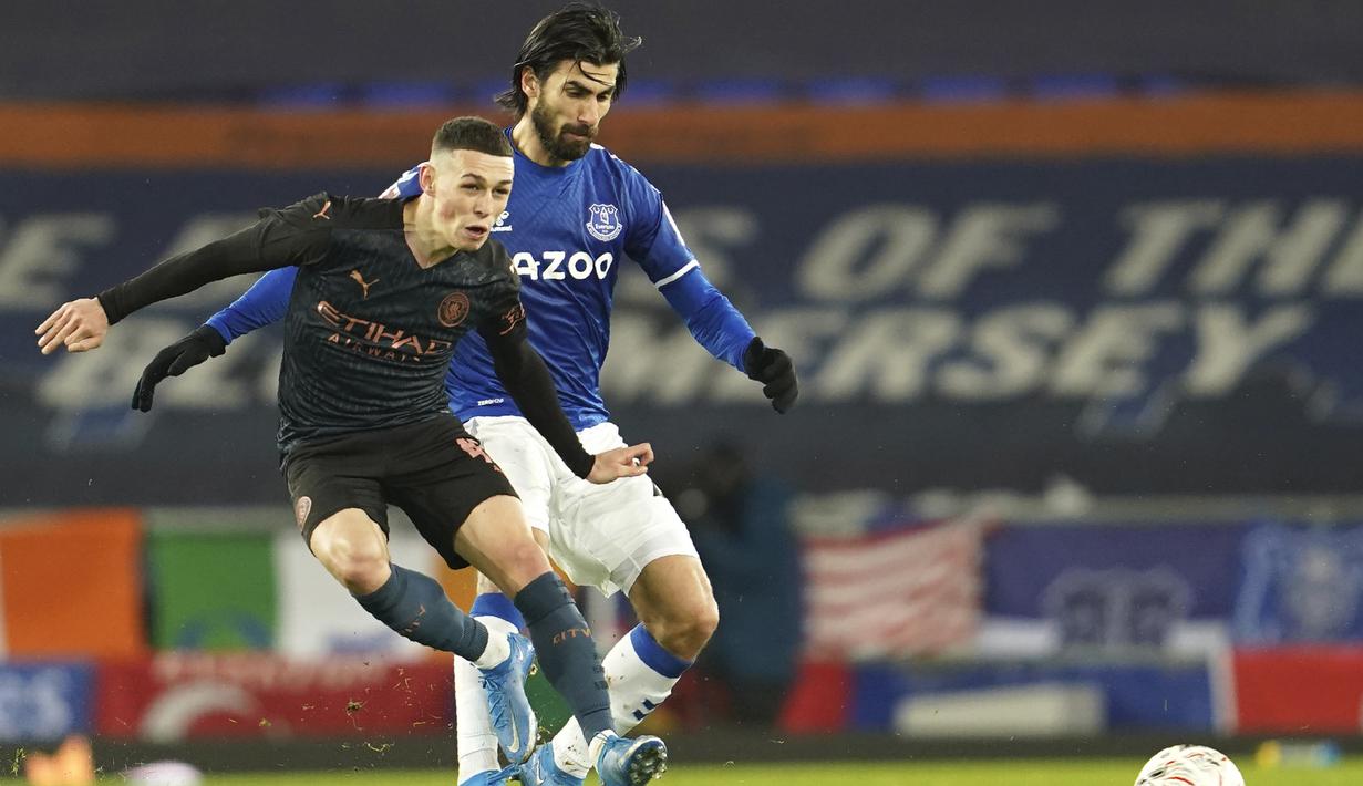 Gelandang Manchester City, Phil Foden (kiri) melepaskan tendangan di depan gelandang Everton, Andre Gomes dalam laga perempatfinal Piala FA 2020/2021 di Goodison Park, Liverpool, Sabtu (20/3/2021). Manchester City menang 2-0 atas Everton. (AP/Jon Super/Pool)