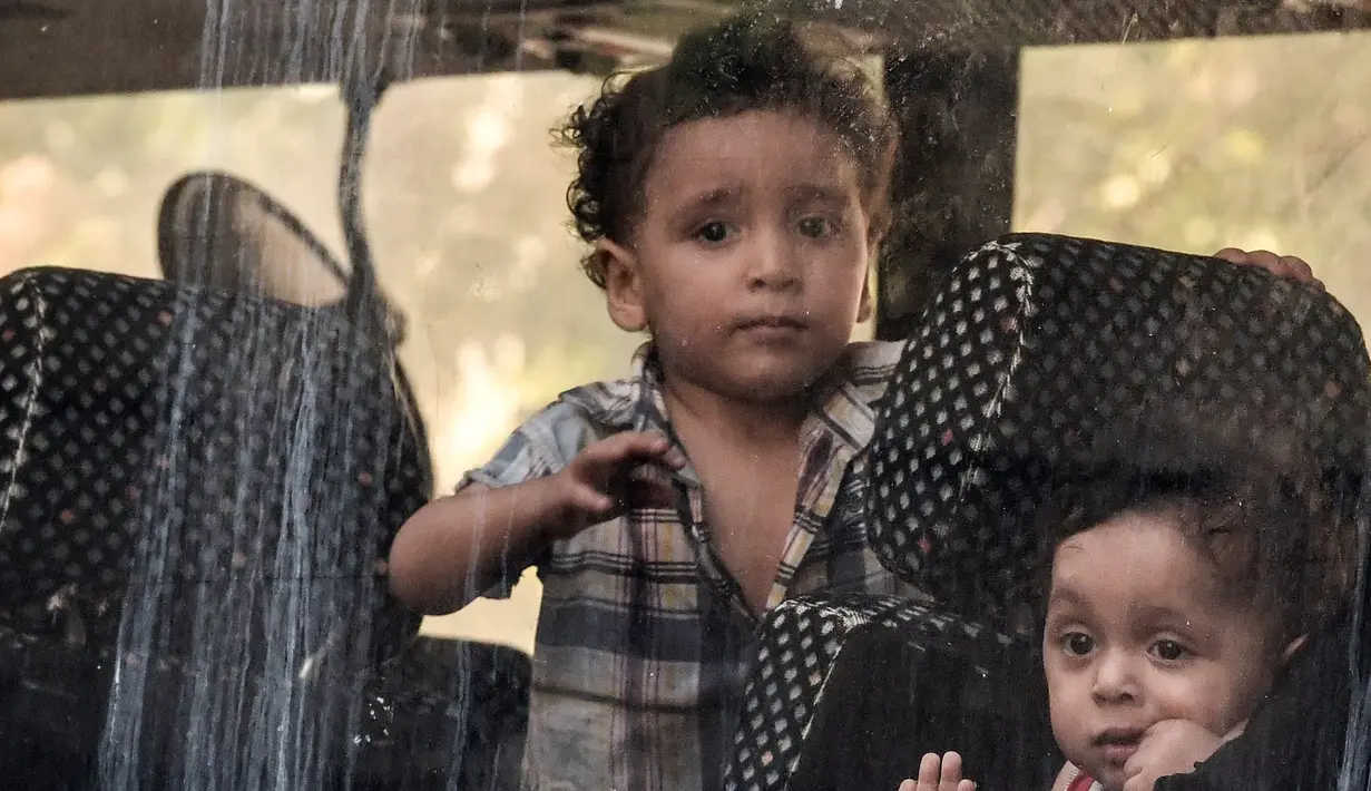 Anak-anak imigran terlihat di jendela bus selama operasi polisi di pusat Athena, Yunani (19/9/2019). Pembersihan para imigran di pusat kota tersebut digerakkan oleh pemerintah konservatif yang baru. (AFP Photo/Louisa Gouliamaki)