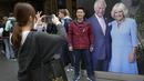 Seorang turis berpose di samping potret besar Raja Charles III dan Ratu Camilla  yang dipajang di Stasiun Kings Cross di London, Senin, 1 Mei 2023. Penobatan Raja Charles III akan berlangsung di Westminster Abbey pada 6 Mei. (AP Photo/Kirsty Wigglesworth)