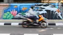 Pengendara sepeda motor melintas di samping mural bertema biota laut yang menghiasi dinding di kawasan Cideng, Jakarta, Rabu (29/11/2023). Mural dibuat guna memperindah sekaligus penataan kawasan Kelurahan Cideng, Jakarta Pusat. (Liputan6.com/Herman Zakharia)
