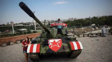 Suporter Red Star Belgrade berpose di tank T-55 yang terparkir di tribun utara Stadion Rajko Mitic, Belgrade, Serbia, Selasa (27/8/2019). Kehadiran tank tersebut memicu protes dari pihak Kroasia yang sempat berperang merebut kemerdekaannya dari Yugoslavia. (OLIVER BUNIC/AFP)