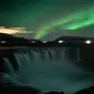 Langit berhias aurora borealis atau Cahaya Utara terlihat di atas air terjun Godafoss di Thingeyjarsveit, Islandia, 14 Oktober 2018. Lukisan abstrak alam semesta dari tabrakan spektrum warna Aurora Borealis begitu spektakuler. (Mariana SUAREZ/AFP)