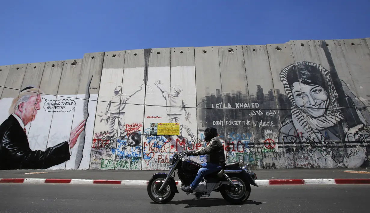 Seorang wanita mengambil gambar grafiti Presiden AS Donald Trump di tembok pemisah Israel - Palestina di kota Bethlehem (4/8).  (AFP Photo/Musa Al Shaer)