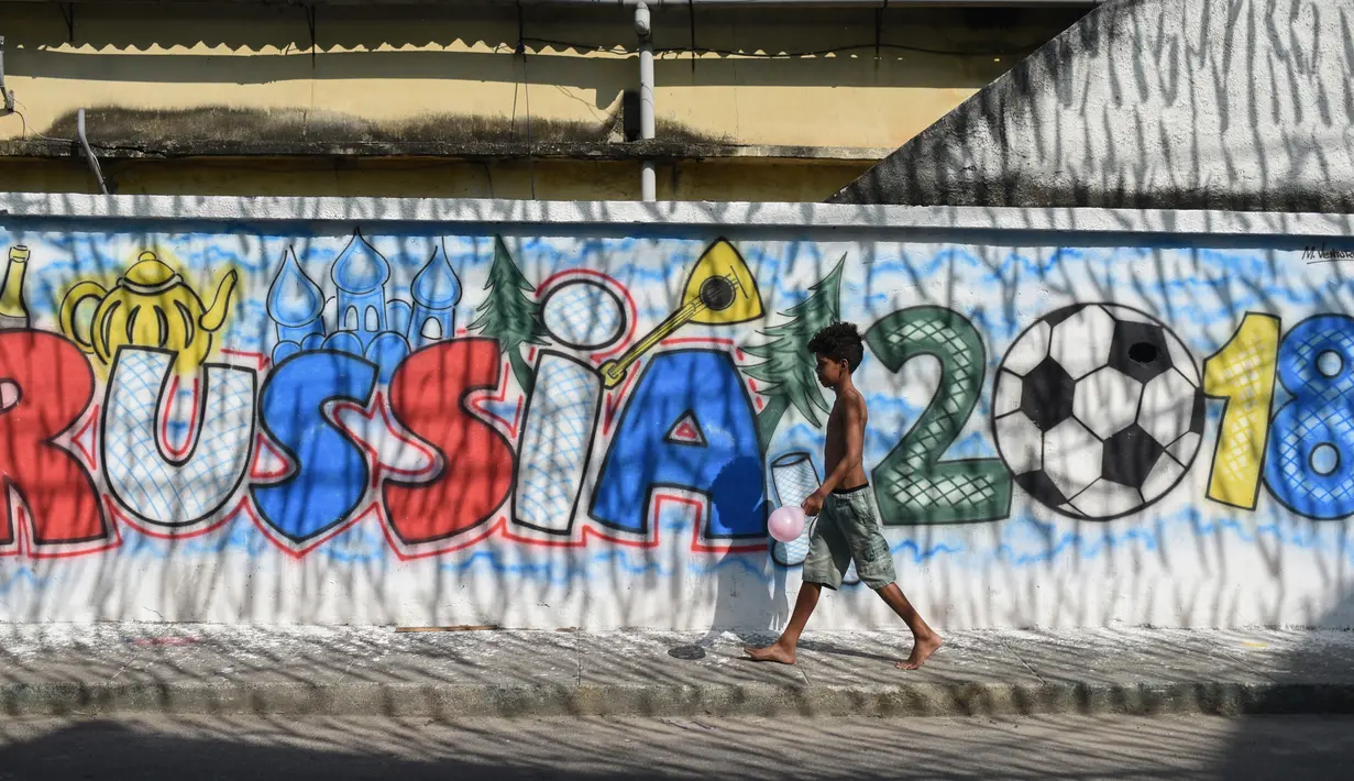Seorang anak laki-laki melewati mural Piala Dunia 2018 di dinding jalanan Camboata, Rio de Janeiro, Brasil, Kamis (31/6). (Fabio TEIXEIRA/AFP)