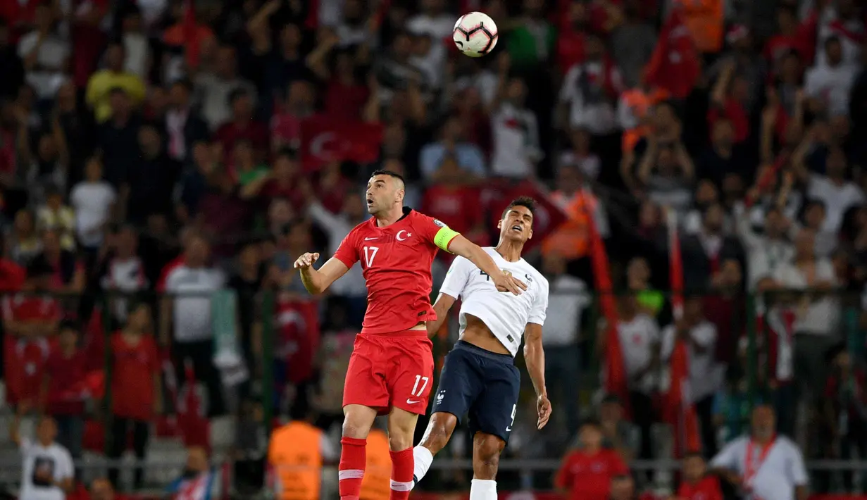 Striker Turki, Burak Yilmaz, duel udara dengan bek Prancis, Raphael Varane, pada laga kualifikasi Piala Eropa 2020 di Stadion Buyuksehir Belediyesi, Minggu (9/6). Turki menang 2-0 atas Prancis. (AFP/Bulent Kilic)