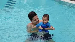 Ardina dan suami sedang menikmati menjadi orang tua. Tak hanya bermain bersama ular, Arie juga ajak si bungsu untuk berenang. (Instagram.com/ardinarasti6)