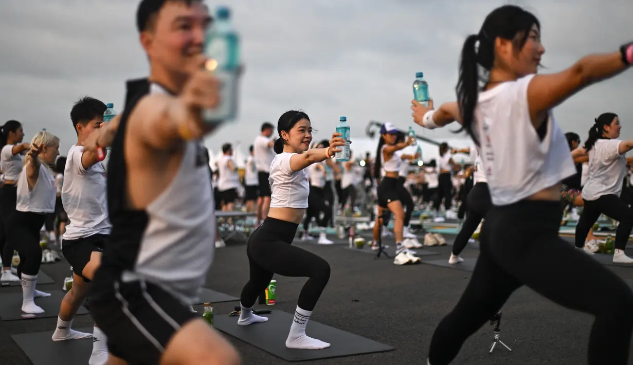 Dengan merentangkan ujung jari mereka ke langit yang memerah, ratusan penggemar yoga menggelar matras mereka di landasan pacu bandara utama Bangkok, mempraktikkan gerakan downward dog saat penerbangan pagi hari bergemuruh di atas kepala. (MANAN VATSYAYANA / AFP)