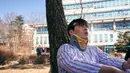 Jung Yeol tampak termenung di bawah pohon dengan baju pasien. Terlihat juga sejumlah luka di tubuhnya. (Foto: Mindmark via Soompi)