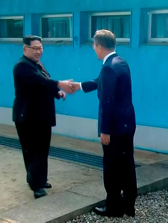 Pemimpin Korea Utara Kim Jong-un dan Presiden Korea Selatan Moon Jae-in berjabat tangan untuk memulai pertemuan bersejarah mereka di atas garis demarkasi Zona Demiliterisasi (DMZ), Panmunjom, Jumat (27/4). (Korea Broadcasting System via AP)