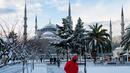 Orang-orang berjalan di alun-alun yang tertutup salju di depan Masjid Biru di Istanbul pada 23 Januari 2022. Badai musim dingin dan hujan salju tetap berlaku di sebagian besar wilayah Turki, menyebabkan penutupan jalan antara ribuan desa dan kota di banyak daerah. (Yasin AKGUL / AFP)