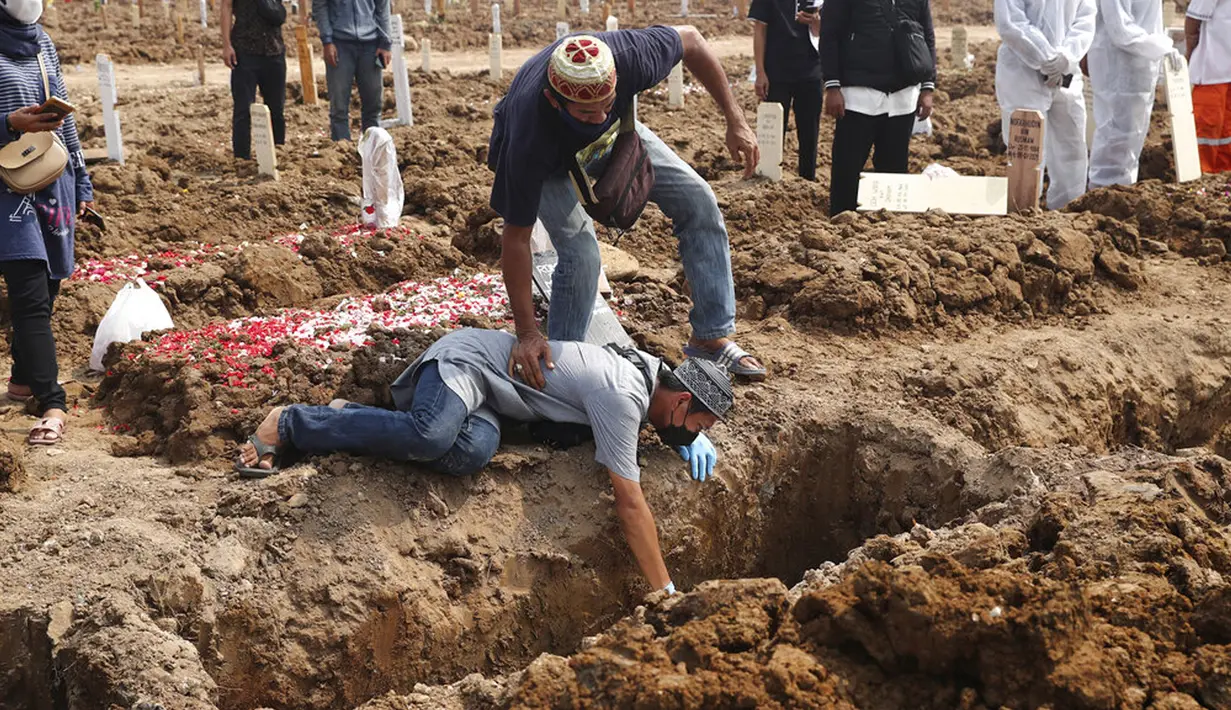 Seorang pria jatuh ke tanah saat dia menangis selama pemakaman kerabat yang meninggal karena COVID-19 di TPU Rorotan, Jakarta, Rabu (7/7/2021). Indonesia menghadapi gelombang kedua COVID-19. (AP Photo/Tatan Syuflana)