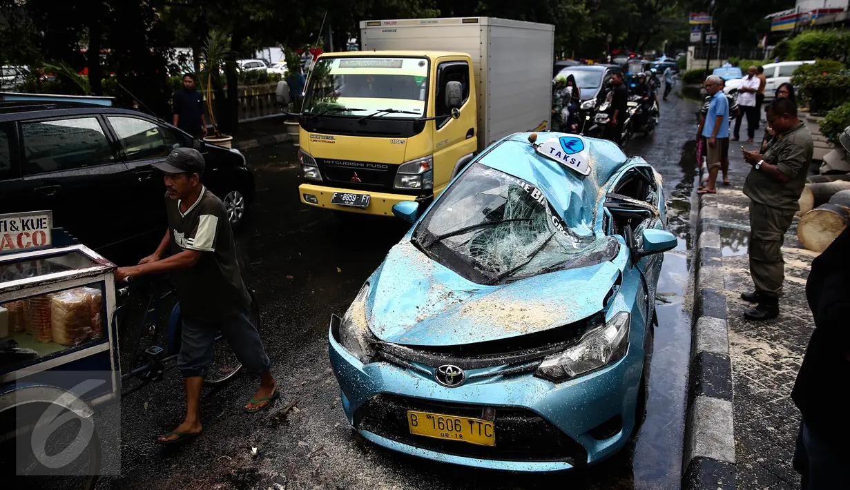 Satu unit taksi ringsek tertimpa pohon tumbang di Jalan Taman Kebon Sirih, Jakarta, Selasa (30/8). Pohon yang batangnya besar tersebut tumbang akibat hujan deras disertai angin kencang yang melanda Jakarta tadi siang. (Liputan6.com/Faizal Fanani) 