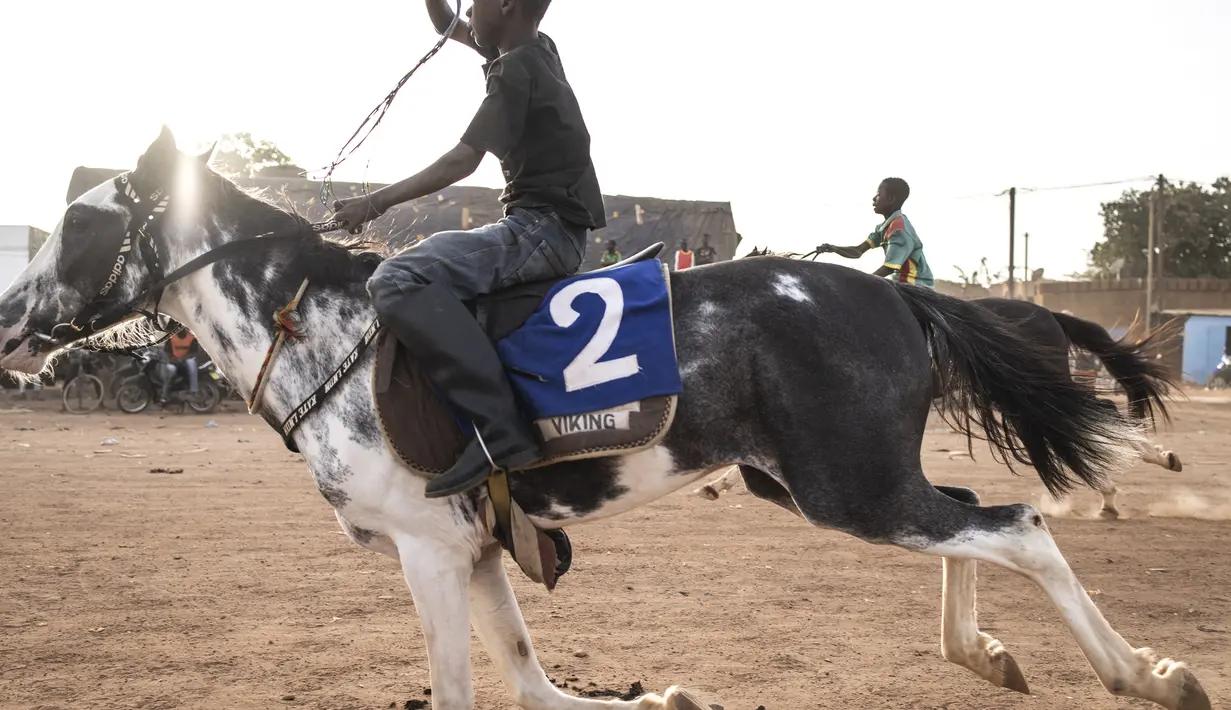 Seorang joki muda berlomba dalam acara pacuan kuda di Ouagadougou (30/1/2022). Koboi terkenal memenangkan jutaan Franc Afrika Barat dari balapan dan diam-diam melatih kuda di malam hari untuk melakukan dressage, beberapa bahkan menyebut diri mereka koboi dan berpakaian sesuai. (AFP/John Wessels)