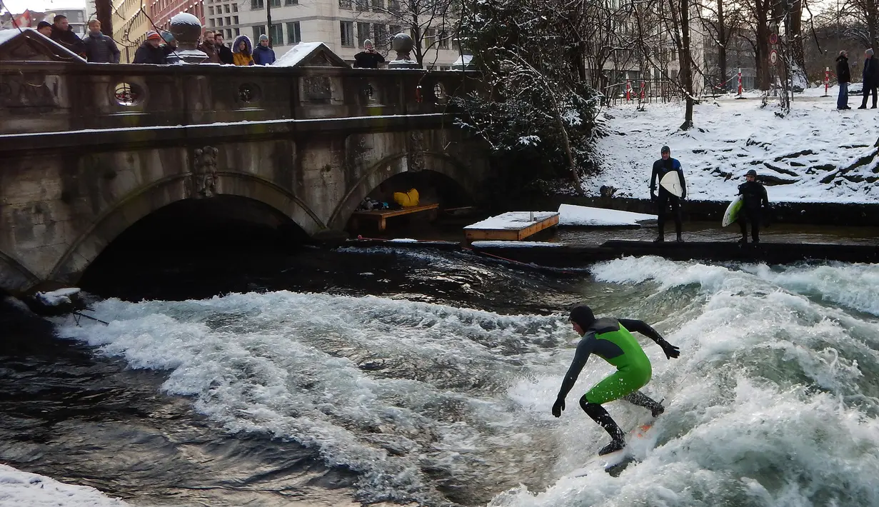 Sejumlah orang dari atas jembatan menyaksikan para pelancar beraksi menaklukkan ombak Sungai Eisbach di Munich, Jerman, 4 Januari 2017. Sungai Eisbach selalu dipadati para peselancar sepanjang tahun, tidak bergantung musim. (Mark RALSTON/AFP)