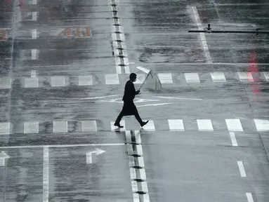 Seorang pria berjalan di tengah hujan yang dibawa oleh Topan Mindulle di Tokyo, Jepang, Jumat (1/10/2021). Topan Mindulle sedang bergerak di lepas pantai Jepang. (AP Photo/Eugene Hoshiko)